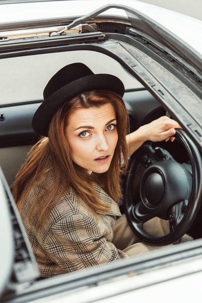 μεγάλη γωνία προβολής γυναίκας σε μαύρο καπέλο που κάθεται στο τιμόνι αυτοκινήτου - Φωτογραφία, εικόνα
