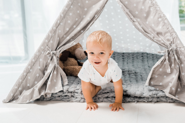 smiling adorable toddler sitting in baby wigwam with fluffy teddy bear toy - Fotó, kép