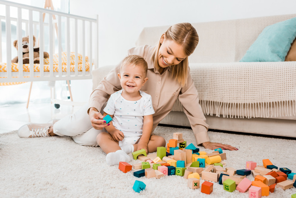 entzückendes Kleinkind spielt mit bunten Würfeln und Mutter im Kinderzimmer - Foto, Bild