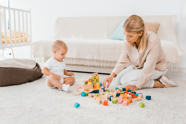 entzückendes Kleinkind spielt mit bunten Würfeln und Mutter im Kinderzimmer - Foto, Bild