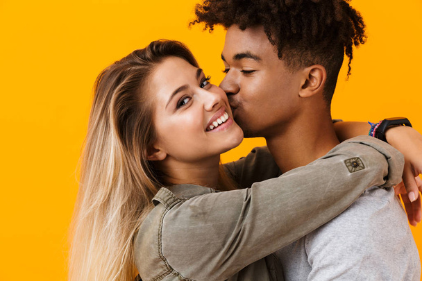 Image of happy cute young loving couple posing isolated over yellow background hugging kissing. - Foto, afbeelding