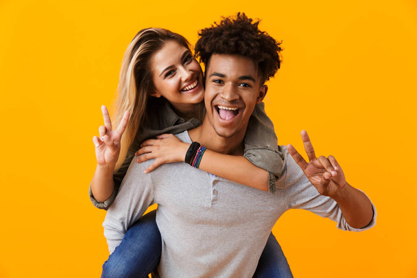 Image of happy cute young loving couple posing isolated over yellow background hugging showing peace gesture. - Foto, Bild