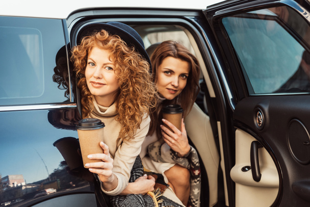 jolies femmes adultes avec tasses à café jetables regardant de la voiture à la rue
 - Photo, image