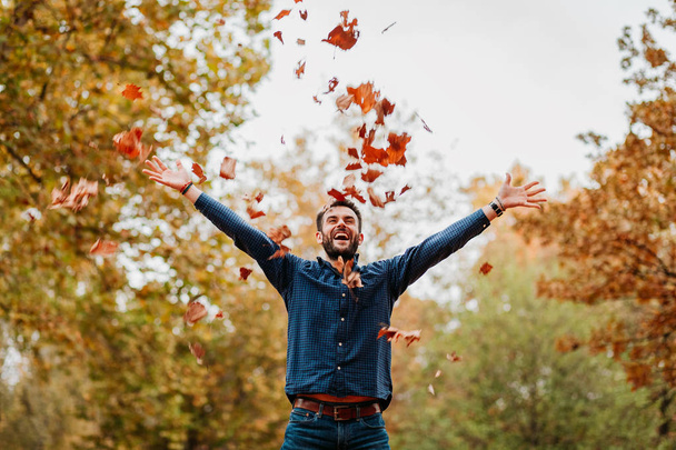 Молодий чоловік кидає осіннє листя в повітря
 - Фото, зображення