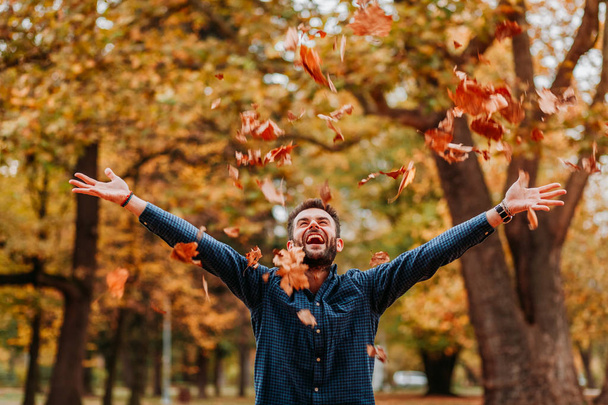 Genç adam gökyüzüne sonbahar yaprakları atıyor. - Fotoğraf, Görsel