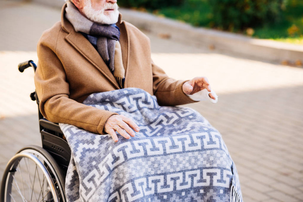 bijgesneden schot voor senior gehandicapte man in rolstoel met plaid op benen op straat - Foto, afbeelding