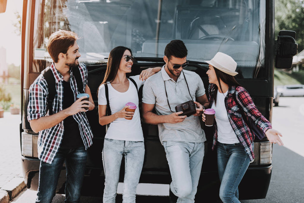 Молодые люди пьют кофе перед автобусом. Группа улыбающихся друзей с рюкзаками, стоящими вместе и разговаривающими. Концепция путешествий, туризма и людей. Счастливые путешественники на летних каникулах
 - Фото, изображение
