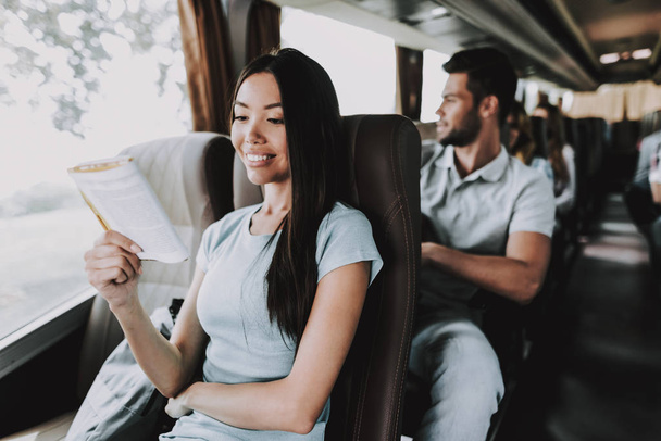 Young Smiling Woman Reading Book in Tourist Bus. Happy Beautiful Girl Sitting on Passenger Seat of Tour Bus and Reading Book. Traveling, Tourism and People Concept. Happy Travelers on Trip - Foto, afbeelding