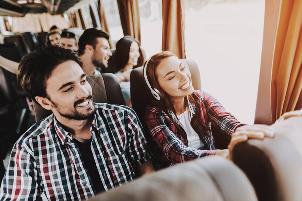 Young Smiling Couple Traveling on Tourist Bus. Handsome Man and Beautiful Woman in Headphones Relaxing on Passenger Seats of Tour Bus. Traveling, Tourism and People Concept. Happy Travelers on Trip - Foto, afbeelding