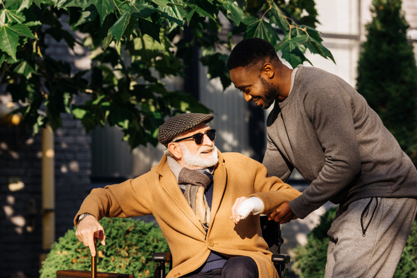 щасливий афроамериканський чоловік допомагає старшому інваліду вставати з інвалідного візка на вулиці
 - Фото, зображення