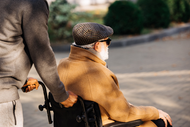 cropped shot of senior disabled man in wheelchair and nurse riding on street - Fotoğraf, Görsel
