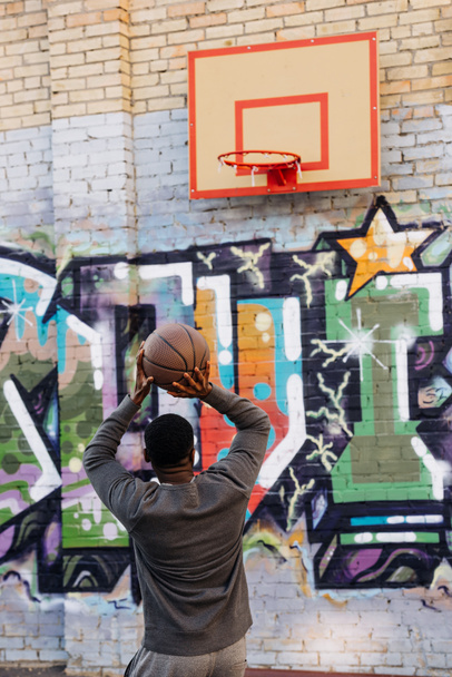 handsome african american man throwing basketball ball into ring on street - Photo, Image