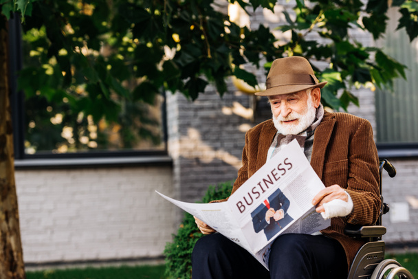 senior disabled man in wheelchair reading business newspaper on street - Фото, изображение