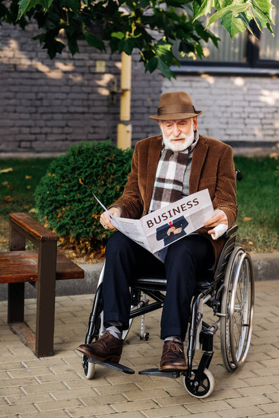 przystojny senior niepełnosprawny człowiek na wózku inwalidzkim, czytania gazety biznes na ulicy - Zdjęcie, obraz