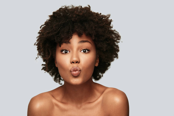 beautiful young African woman making face with kiss while standing against grey background - Φωτογραφία, εικόνα
