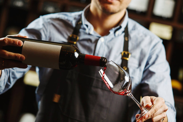 Male sommelier pouring red wine into long-stemmed wineglasses. - Фото, зображення