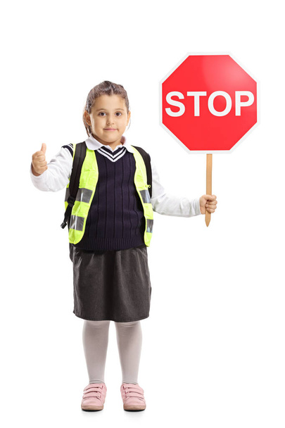 Täyspitkä muotokuva koulutyttö yllään turvaliivi, tilalla stop-merkki ja näyttää peukalot ylös eristetty valkoisella taustalla
 - Valokuva, kuva