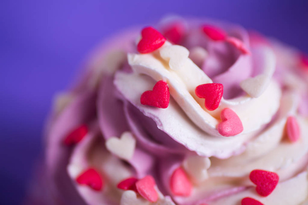 Closeup cupcake with creamy pink and white top decorated with little hearts on purple background. St. Valentine day dessert. - Photo, Image