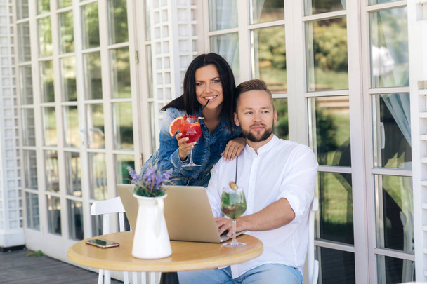 Šťastný manželský pár, Nakupování v internetovém obchodě pomocí přenosného počítače, sedí u stolu v kavárně, dívka objímá muže za ramena. - Fotografie, Obrázek