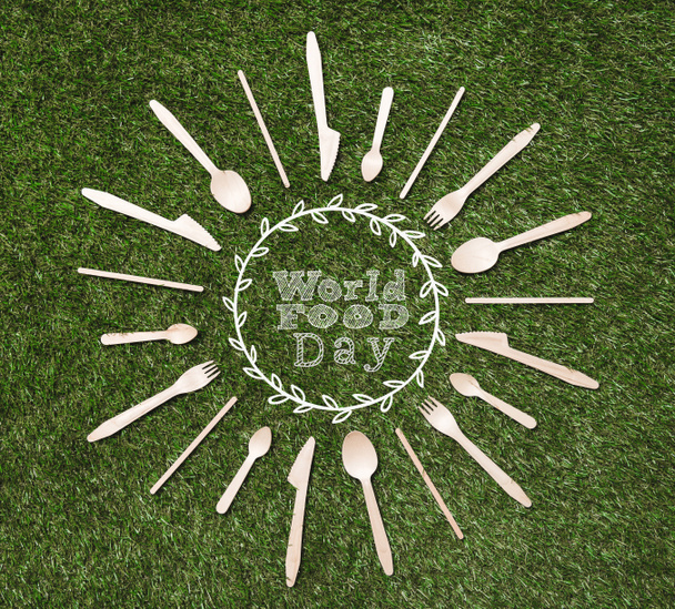 top view of wooden spoons with forks and knives in shape of sun lying on grass, world food day inscription - Photo, Image