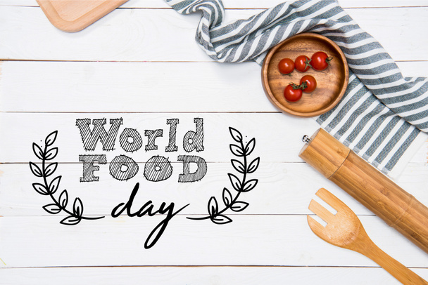 Tomates cereja com espátula de madeira e moedor de sal com toalha de mesa no tampo da mesa, inscrição do dia mundial da comida
 - Foto, Imagem