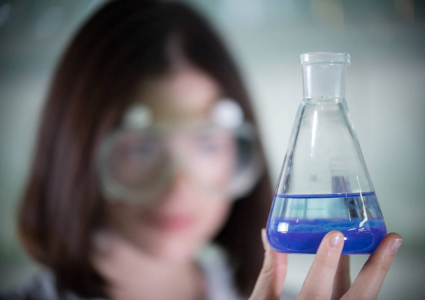化学実験室。笑顔で若い女性が青で、液体をスクラブでフラスコを保持 - 写真・画像