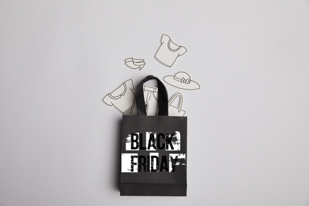 top view of black shopping bag with black friday inscription and paper clothes on grey background - Foto, immagini