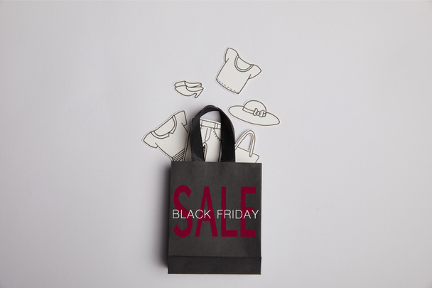 top view of black shopping bag with black friday sale inscription and paper clothes on grey background - Φωτογραφία, εικόνα