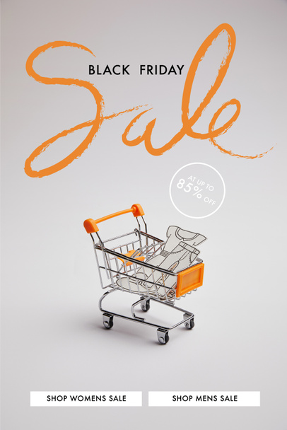 close up view of shopping cart with little goods made of paper on grey background, black friday sale inscription - Фото, изображение