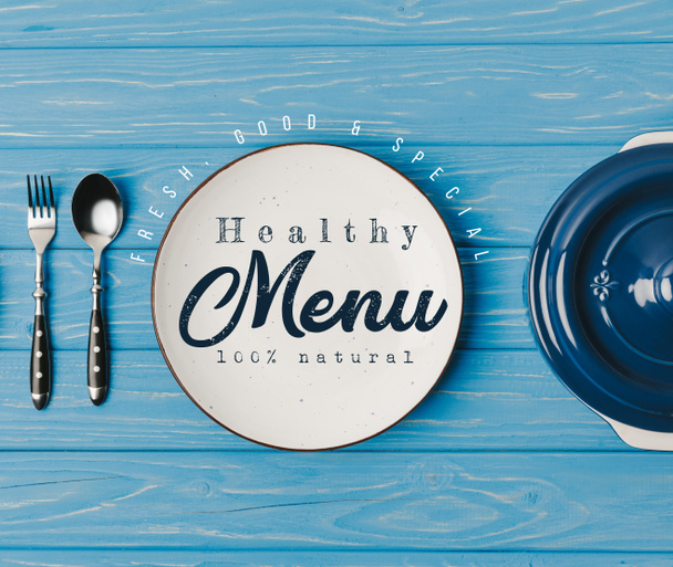 Top uitzicht op vork, lepel en platen op blauwe tafel, gezond menu belettering - Foto, afbeelding