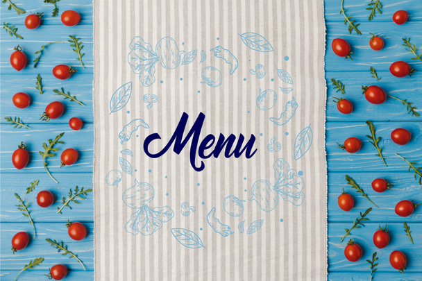 top view of napkin and cherry tomatoes with arugula on blue table, menu lettering - Photo, Image