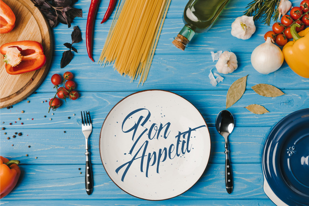 Draufsicht auf Zutaten zum Kochen von Pasta auf blauem Tisch, Guten Appetit Schriftzug - Foto, Bild