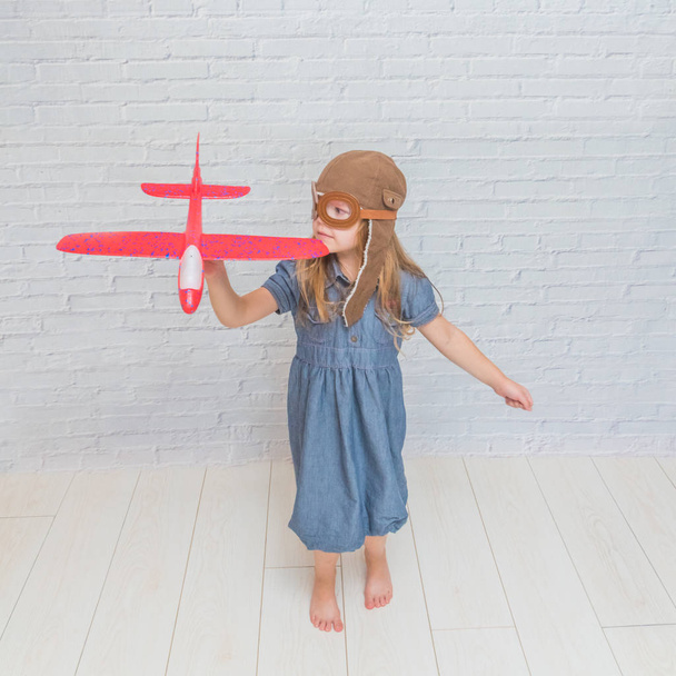 a girl, child in the helmet of the pilot with the aircraft and lights in the glass in front of a white brick wall - Fotoğraf, Görsel