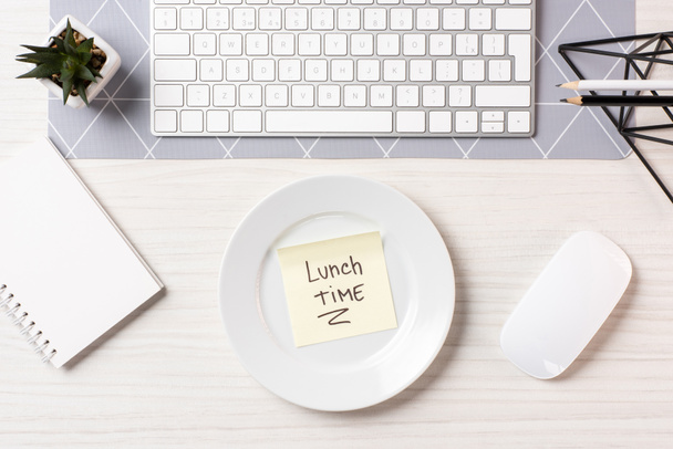 vista superior de la nota con la hora del almuerzo de inscripción en el plato, el ratón de la computadora y el teclado en el lugar de trabajo
 - Foto, imagen