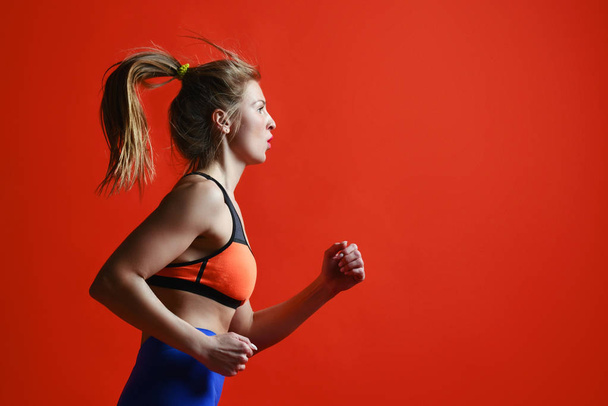 Young woman with fit body jumping and running against red background. - Photo, Image