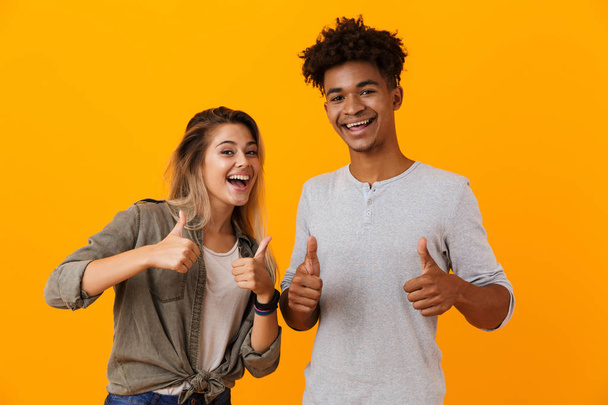 Image of happy cute young loving couple posing isolated over yellow background showing thumbs up. - Foto, Imagem