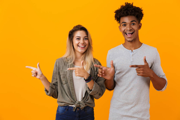 Image of happy cute young loving couple posing isolated over yellow background pointing. - Φωτογραφία, εικόνα