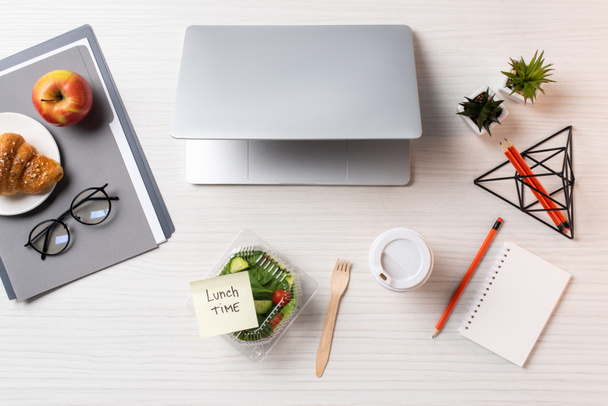 верхний вид контейнера с овощным салатом и липкой запиской с надписью обеденное время, ноутбук и офисные принадлежности на столе
 - Фото, изображение