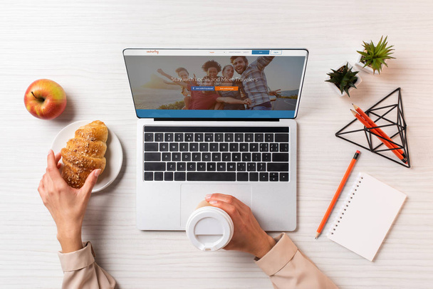 Üzletasszony holding kupa eldobható kávé és croissant laptop couchsurfing weboldal használata közben levágott lövés - Fotó, kép