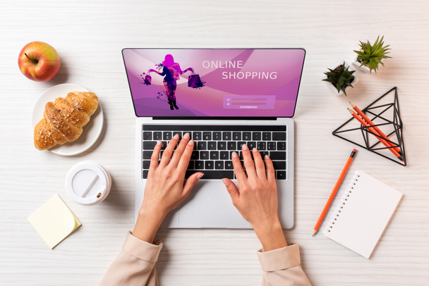 Schnappschuss einer Geschäftsfrau mit Laptop und Online-Shopping-Website am Tisch mit Kaffee, Apfel und Croissant           - Foto, Bild