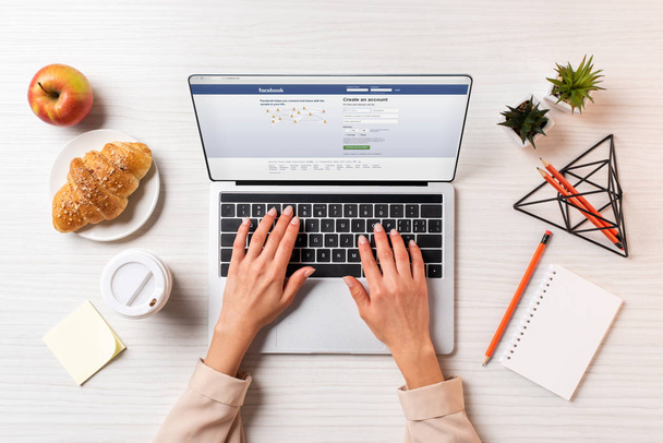 Schnappschuss einer Geschäftsfrau mit Laptop und Facebook-Website am Tisch mit Kaffee, Apfel und Croissant    - Foto, Bild
