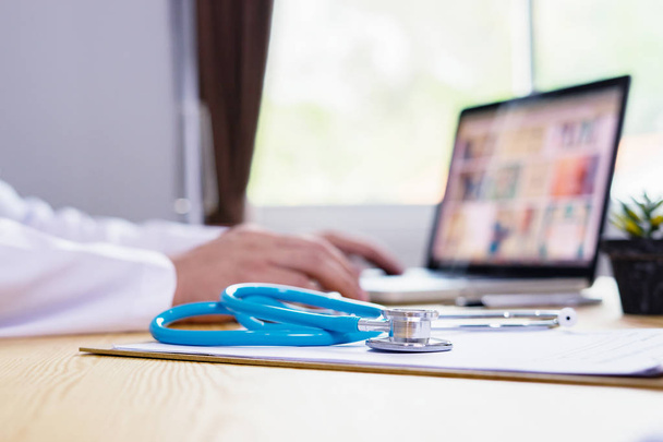 Stethoskop mit Klemmbrett, Arzt am Laptop im Hintergrund - Foto, Bild