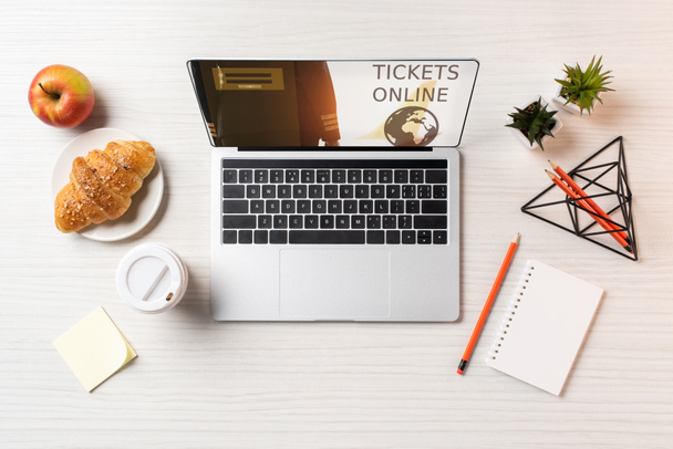 Laptop von oben mit Online-Tickets, Pappbecher, Apfel und Croissant auf dem Tisch im Büro - Foto, Bild