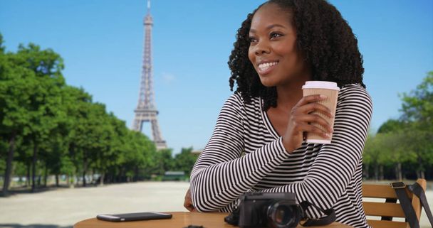 Smiling black woman sitting at outdoor table enjoying view of Eiffel Tower - Zdjęcie, obraz