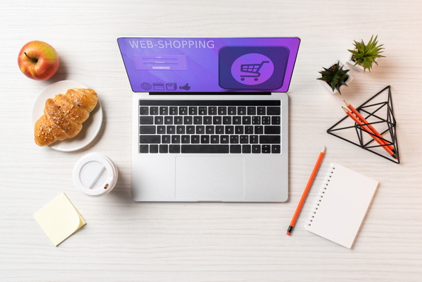 вид зверху на ноутбук з веб-сайтом шопінгу, круасан, яблуко та одноразова чашка кави на офісному столі
    - Фото, зображення