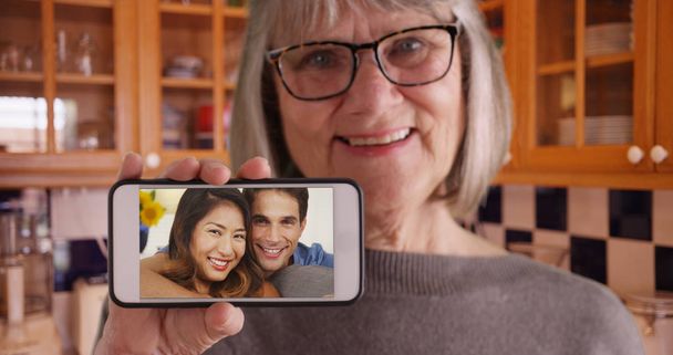 Старушка держит телефон перед камерой во время видеочата с сыном и его девушкой
 - Фото, изображение