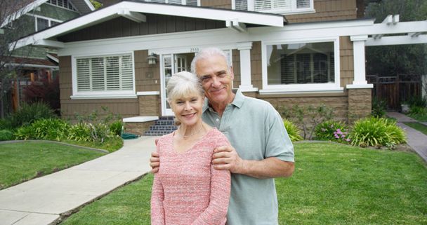 Старша пара стоїть посміхаючись перед новим будинком
 - Фото, зображення