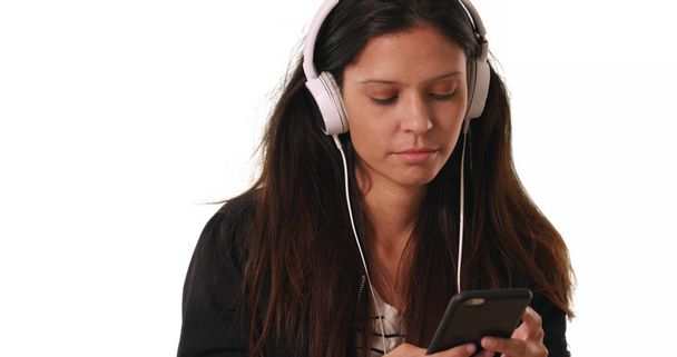 Millennial woman listens to music using smartphone app with headphones on white - Foto, afbeelding