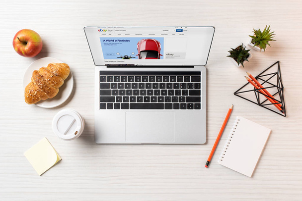 top view of laptop with ebay website, croissant and coffee to go on office table  - 写真・画像