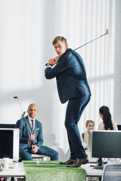 joven hombre de negocios jugando al golf y compañeros de trabajo sentados detrás en la oficina
 - Foto, imagen